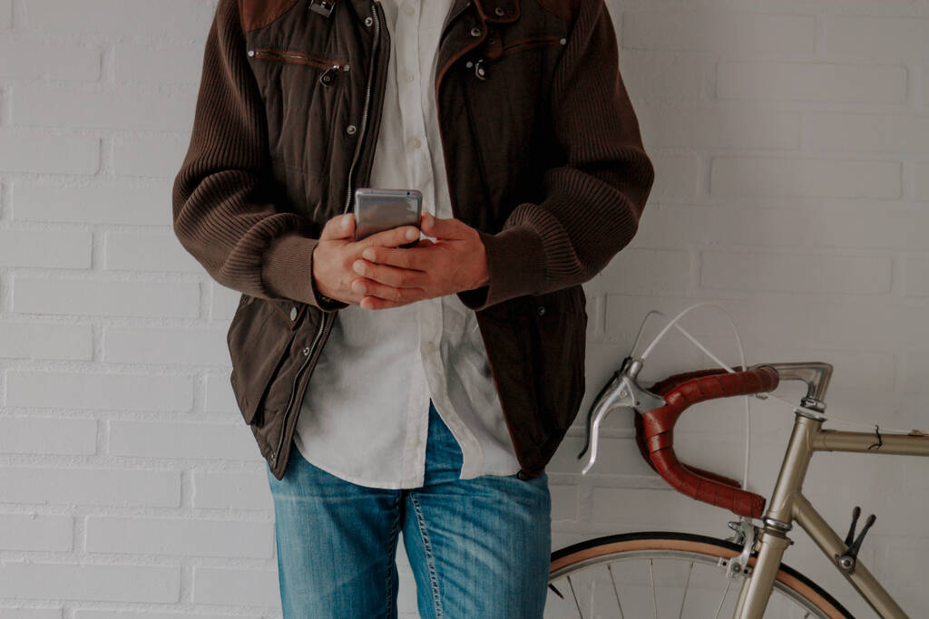man met mobiele telefoon en fiets aan de muur - Foto, afbeelding