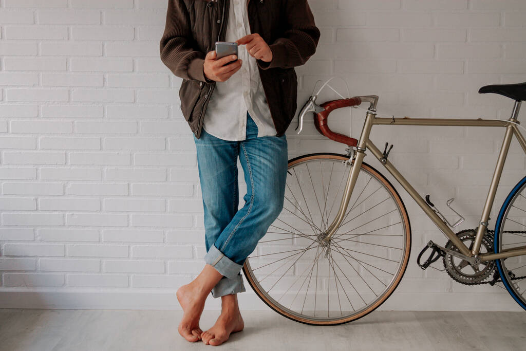 розслаблений чоловік з мобільним телефоном і велосипедом в приміщенні з копіювальним простором
 - Фото, зображення