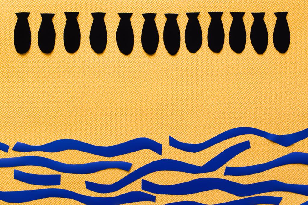 Вид сверху ряда с бумажными бомбами над картонным морем на текстурированном желтом фоне, война в концептуальном виде  - Фото, изображение