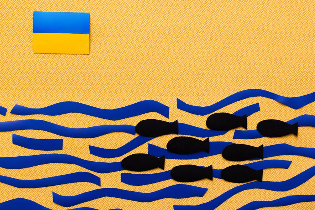 Bovenaanzicht van de Oekraïense vlag boven karton zee en papier bommen op getextureerde gele achtergrond  - Foto, afbeelding
