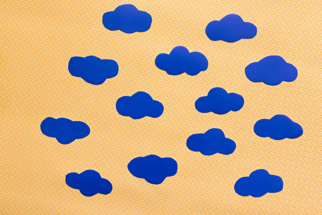 Top view of blue paper clouds on textured yellow background  - Photo, Image