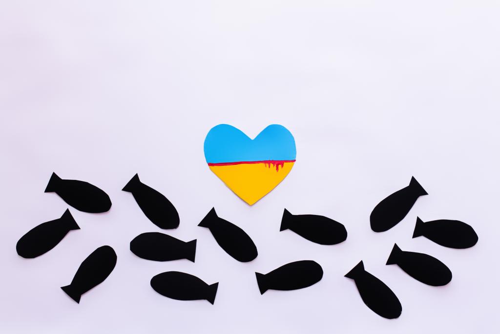 Vue du dessus du drapeau ukrainien avec du sang en forme de coeur près des bombes en papier sur fond blanc  - Photo, image