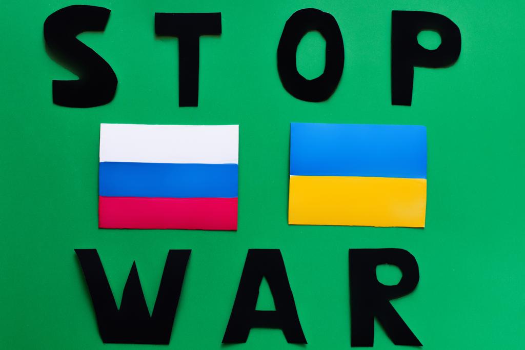 Draufsicht auf Stop War Schriftzug und ukrainische und russische Flaggen auf grünem Hintergrund  - Foto, Bild