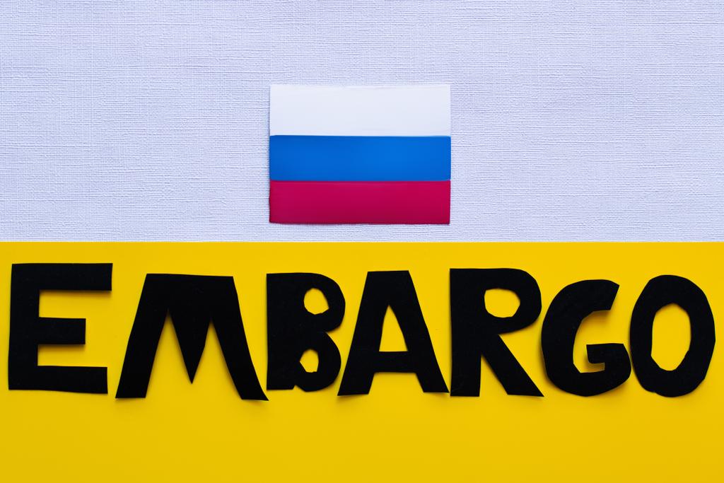Top view of russian flag and embargo lettering on white and yellow background  - Photo, Image