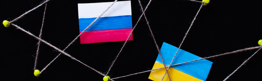 Top view of ukrainian and russian flags near push pins with thread isolated on black, banner - Photo, Image