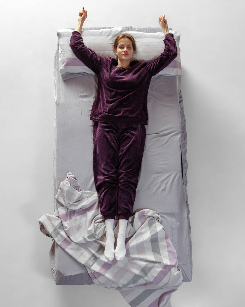 Ritratto creativo di giovane ragazza che indossa abiti da casa color vino, pigiama che dorme nel letto grande. Concetto di salute, interno della casa, tempo di relax, famiglia, sogni - Foto, immagini