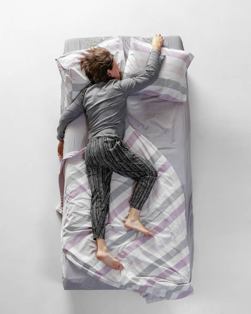 Jeune homme portant des vêtements de maison de couleur grise, pyjama dormant dans un grand lit. Concept de santé, intérieur de la maison, temps de détente, famille, rêves. Vue du dessus - Photo, image