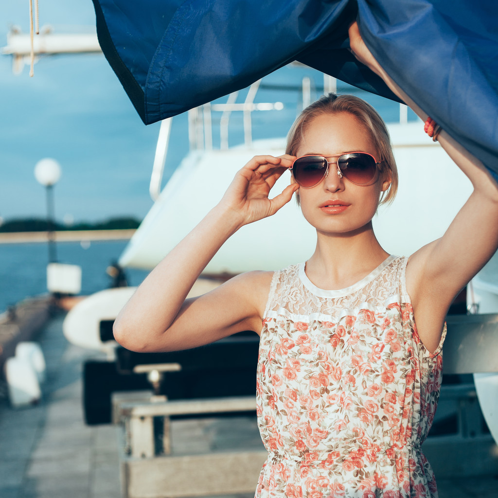 Sarışın kız çiçek elbise ve tekne yelken tutan güneş gözlüğü - Fotoğraf, Görsel