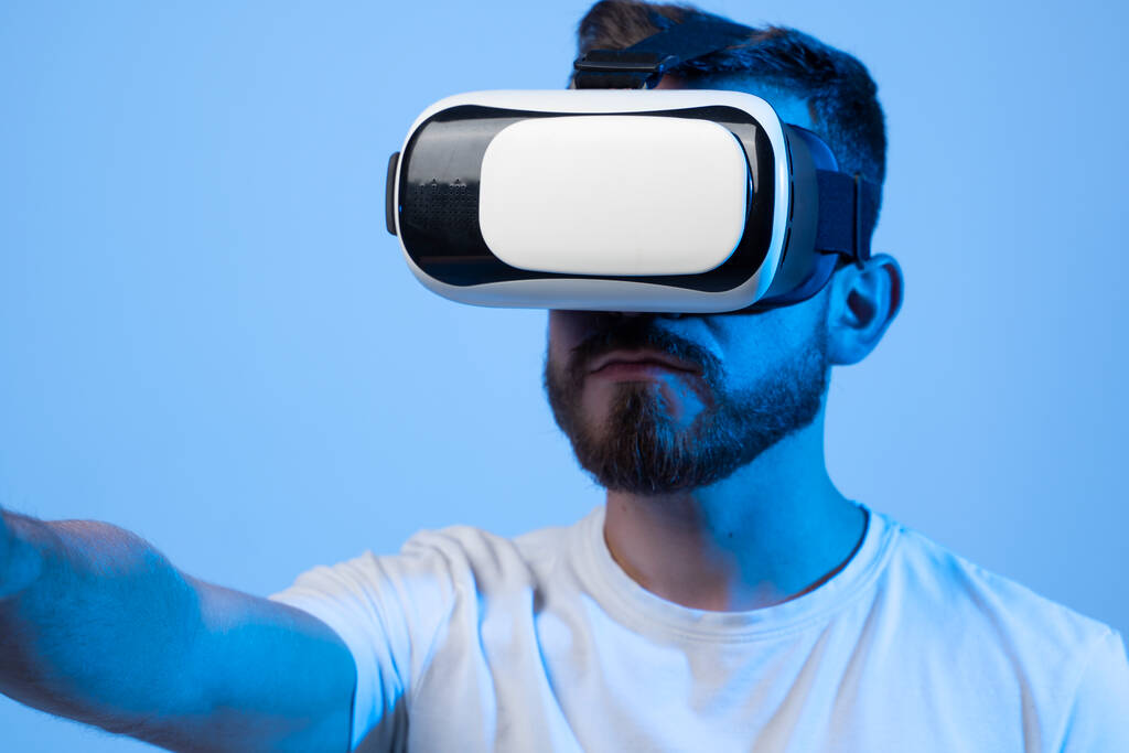 Jeune homme utilisant casque VR casque pour jouer à un jeu de simulation. Regarder la réalité virtuelle vidéo 3d. Homme barbu en lunettes VR regardant autour. - Photo, image