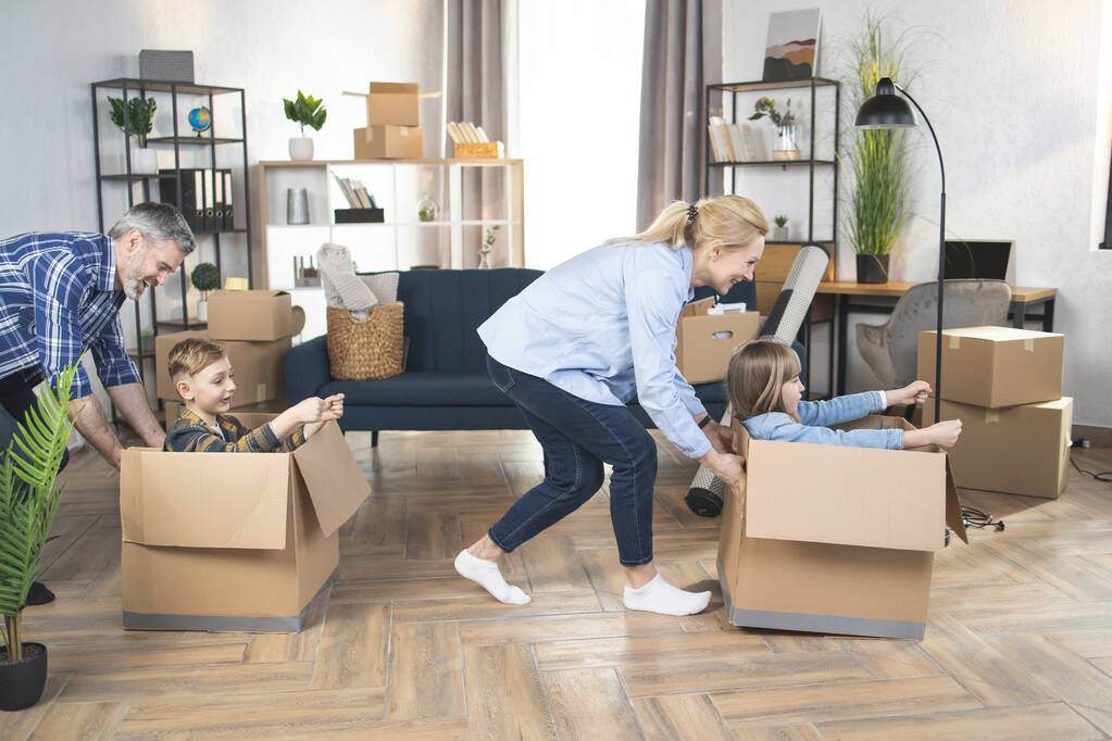Padres y niños caucásicos jugando con cajas durante la reubicación - Foto, Imagen