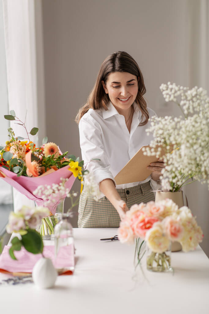glückliche Frau mit Klemmbrett und Blumen im Studio - Foto, Bild