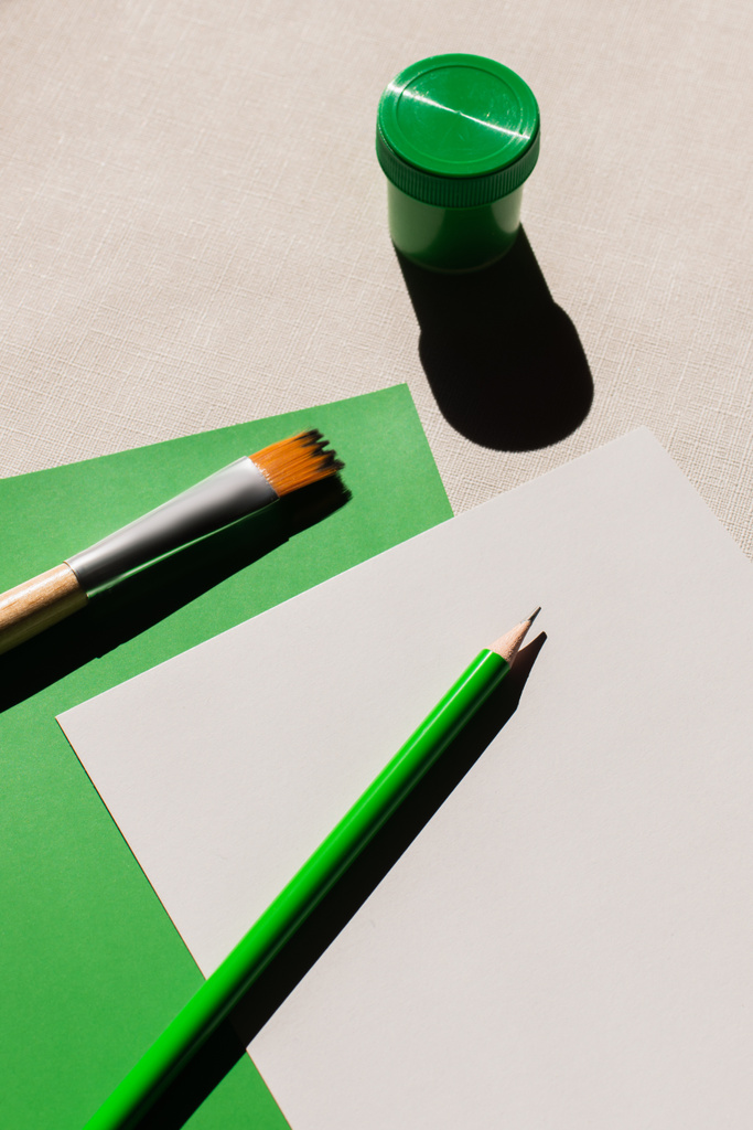 vista superior del pincel y lápiz sobre papel blanco y verde sobre fondo texturizado - Foto, imagen