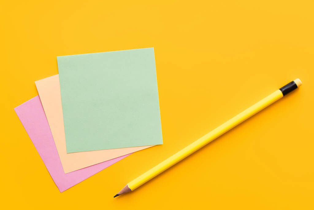 vista superior do lápis perto de notas de papel multicoloridas no fundo amarelo  - Foto, Imagem