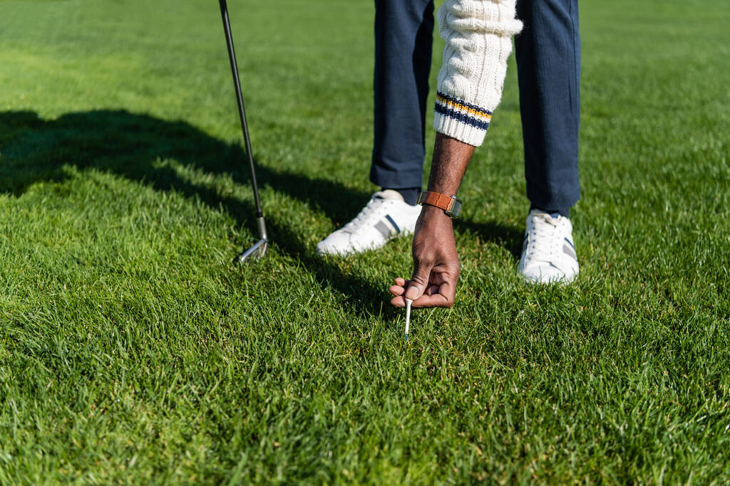 vista recortada de hombre mayor afroamericano colocando camiseta de golf en el césped verde - Foto, Imagen