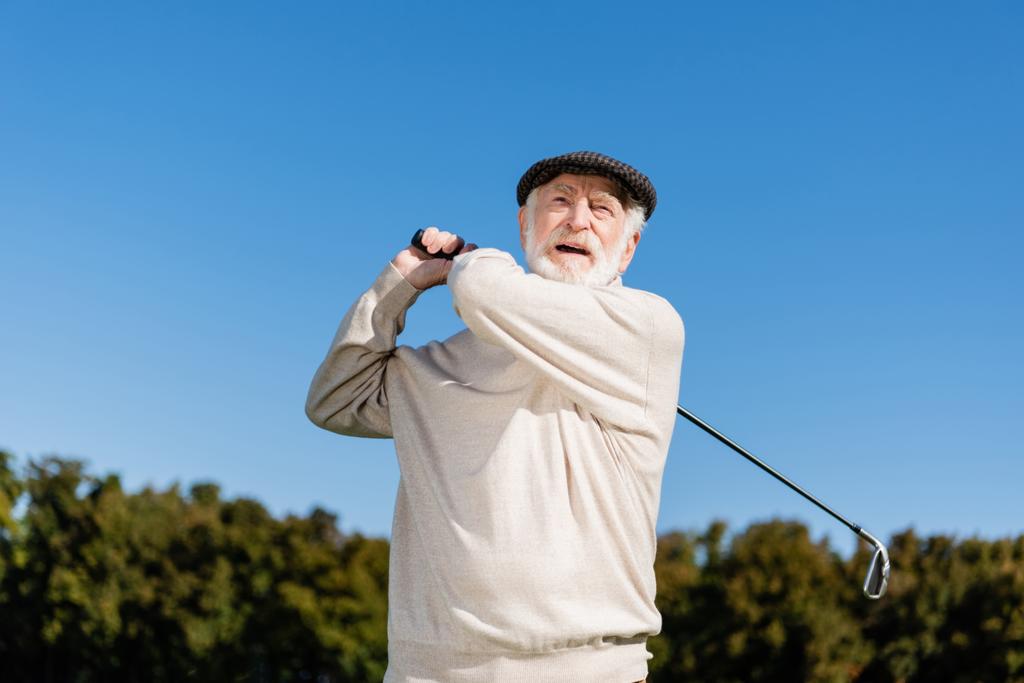 vousatý a starší muž drží golfovou hůl při hraní venku  - Fotografie, Obrázek
