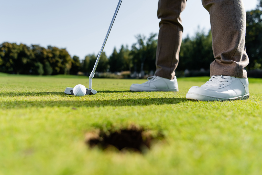 Teilansicht eines Mannes in weißen Turnschuhen beim Golfspielen auf Rasen - Foto, Bild