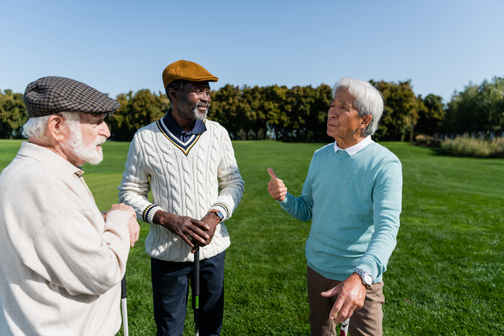 старший азиат жестикулирует и разговаривает с многонациональными друзьями на поле для гольфа - Фото, изображение