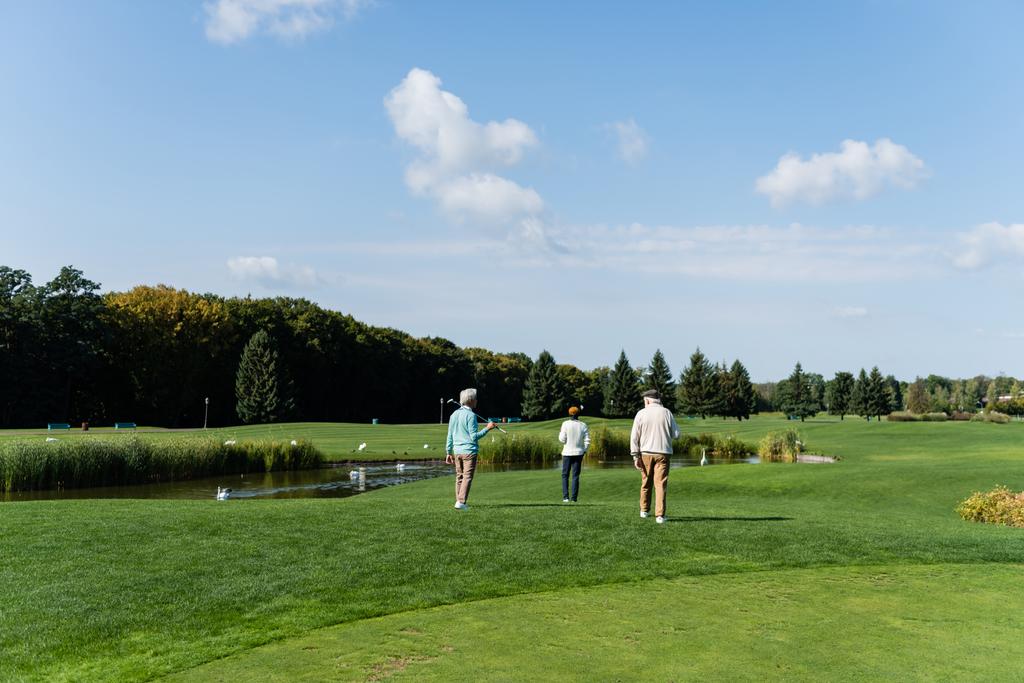 緑の芝生の上をゴルフクラブが池の近くを歩いている  - 写真・画像