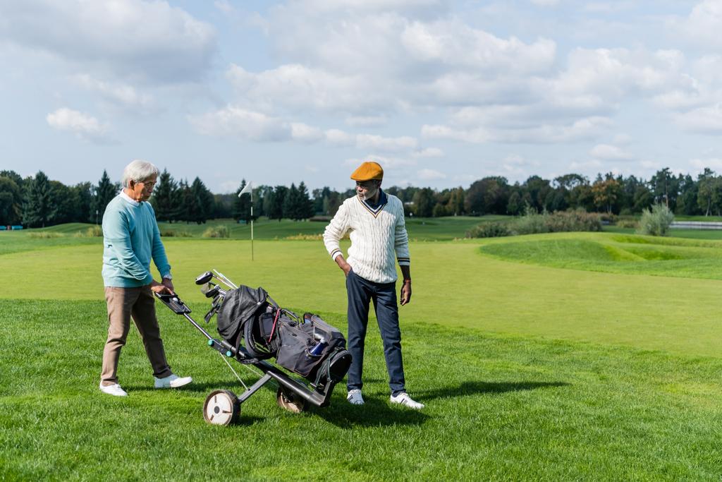 aziatische senior man wandelen met golf kar in de buurt rijke Afrikaanse Amerikaanse vriend  - Foto, afbeelding