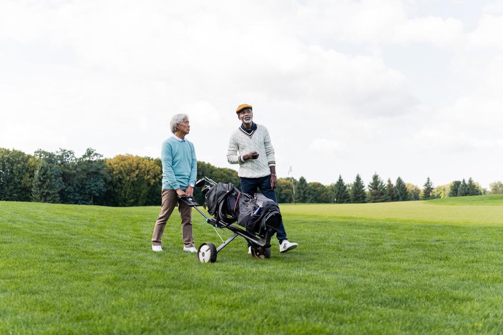 asiatico anziano uomo a piedi con golf carrello vicino africano americano amico  - Foto, immagini
