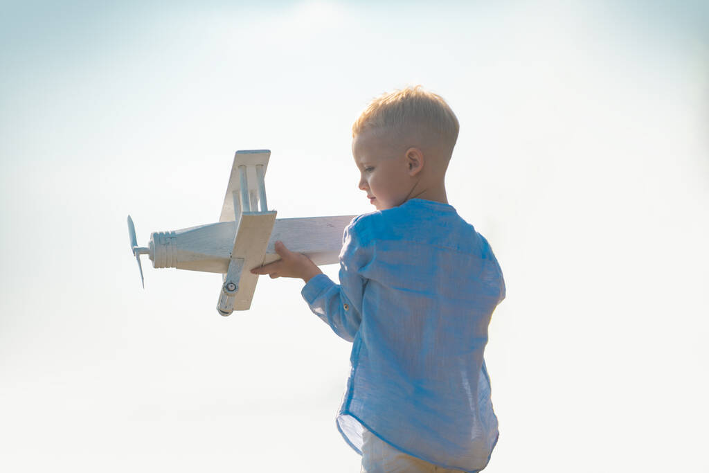 Child boy playing with wooden toy airplane, dream of becoming a pilot. Childrens dreams. Child pilot aviator with wooden plane. Childhood dream imagination concept. - Photo, Image