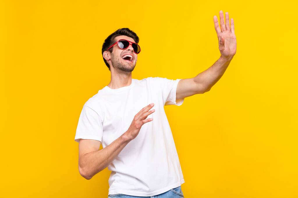 Photo of impressed millennial brunet guy dance wave wear glasses t-shirt isolated on yellow color background - Foto, imagen