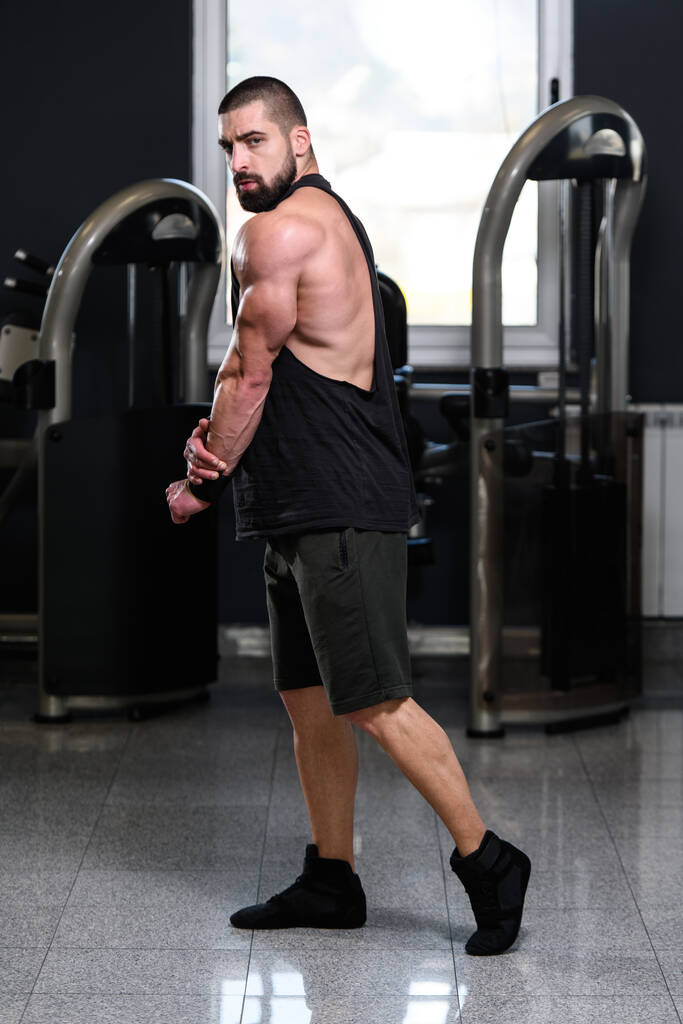Όμορφος νεαρός άνδρας στέκεται ισχυρή στο γυμναστήριο και κάμψη των μυών - Μυϊκή Αθλητική Bodybuilder Fitness Model Posing After Exercises - Φωτογραφία, εικόνα