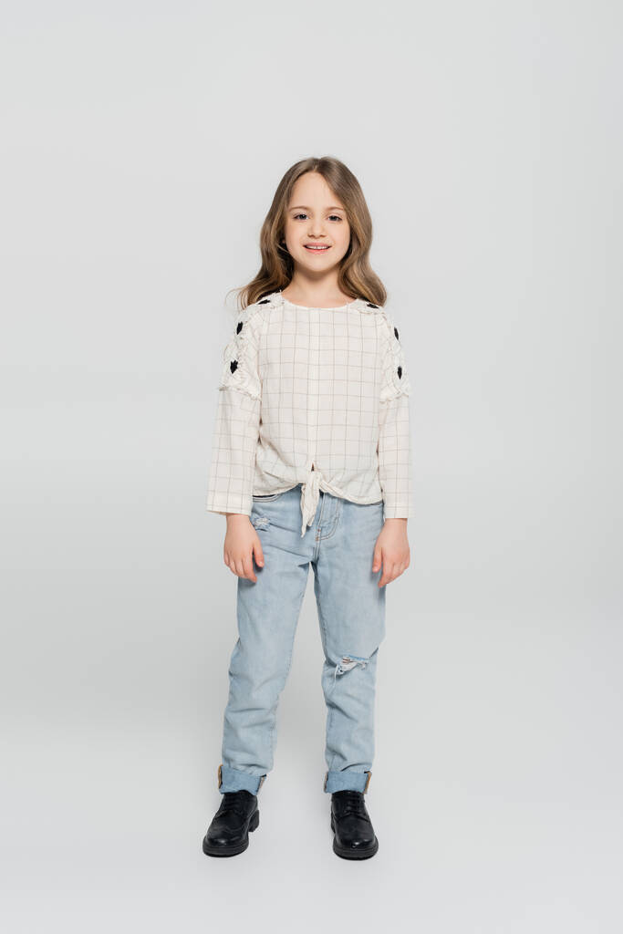 Вид в полный рост улыбающейся девушки в джинсах и белой блузке на сером фоне - Фото, изображение