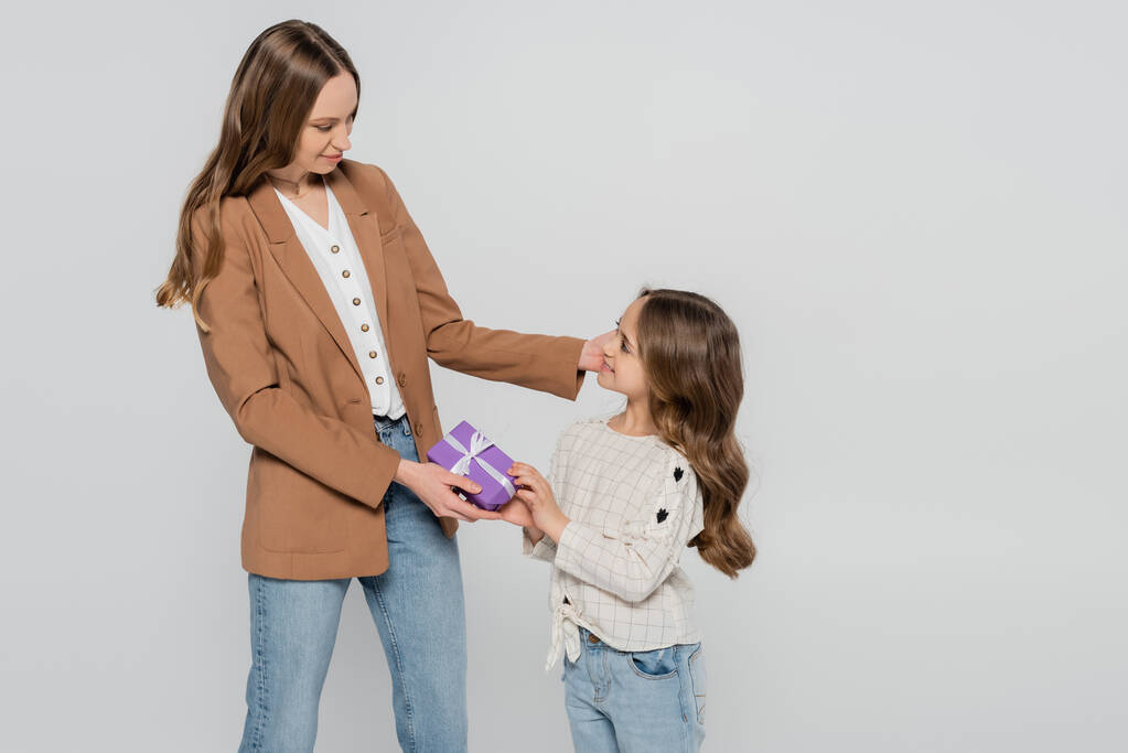 Lächelndes Mädchen überreicht Muttertagsgeschenk an Mutter isoliert auf grau - Foto, Bild