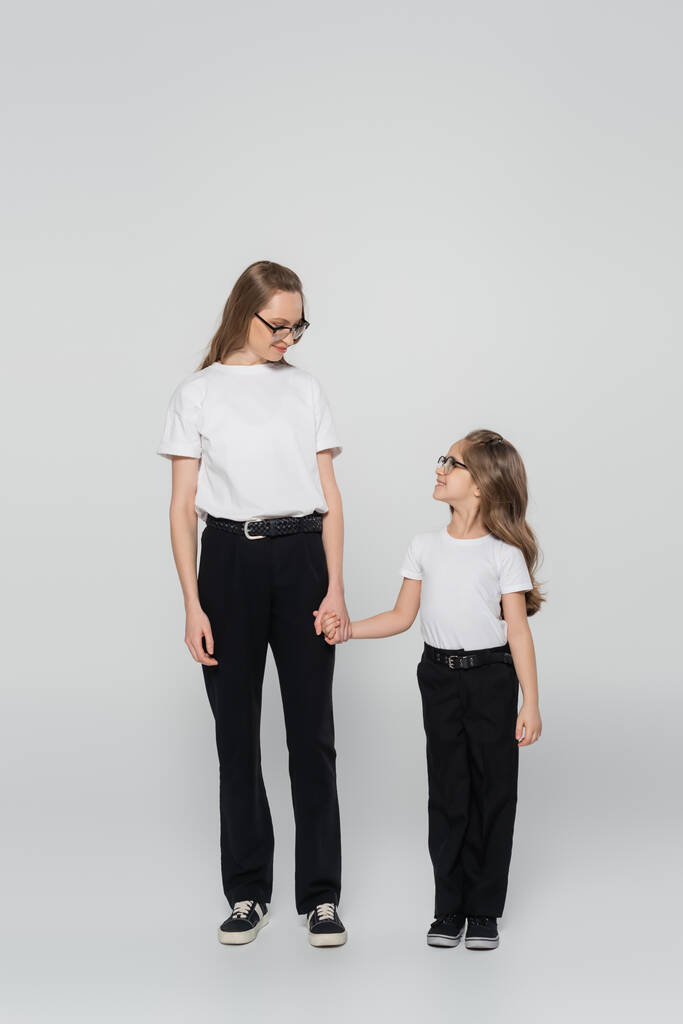 visão de comprimento total de mãe e filho de mãos dadas e olhando uns para os outros em fundo cinza - Foto, Imagem