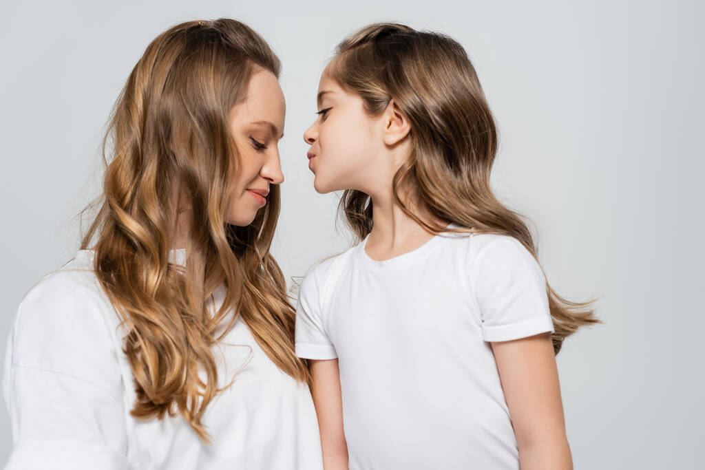 menina em branco t-shirt beijando mãe feliz isolado no cinza - Foto, Imagem