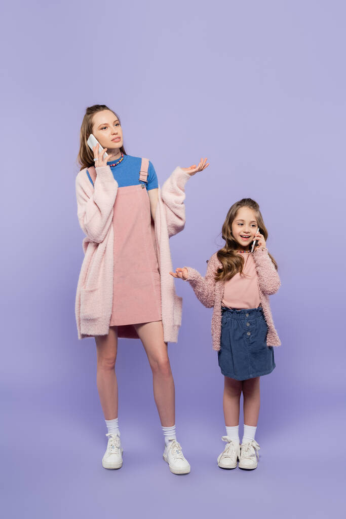 täyspitkä äiti ja tytär puhuvat matkapuhelimissa samalla elehtien violetti - Valokuva, kuva
