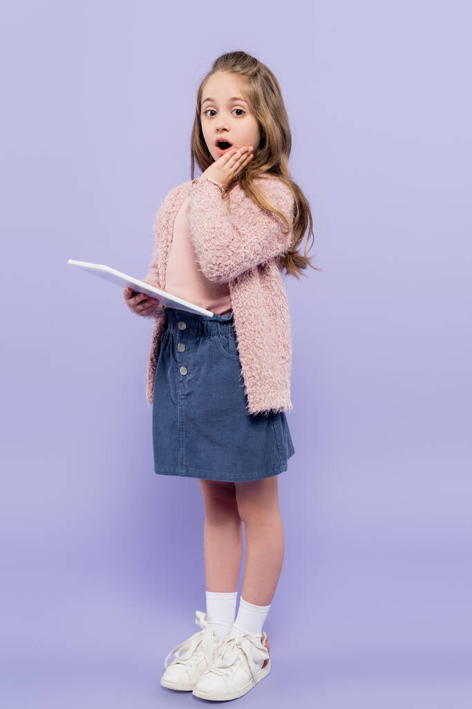 longitud completa de chica sorprendida sosteniendo tableta digital en púrpura - Foto, Imagen