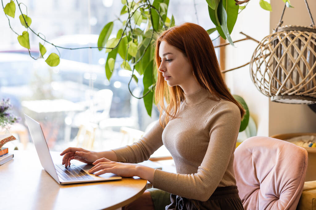 junge rothaarige Frau benutzt Laptop im Café  - Foto, Bild