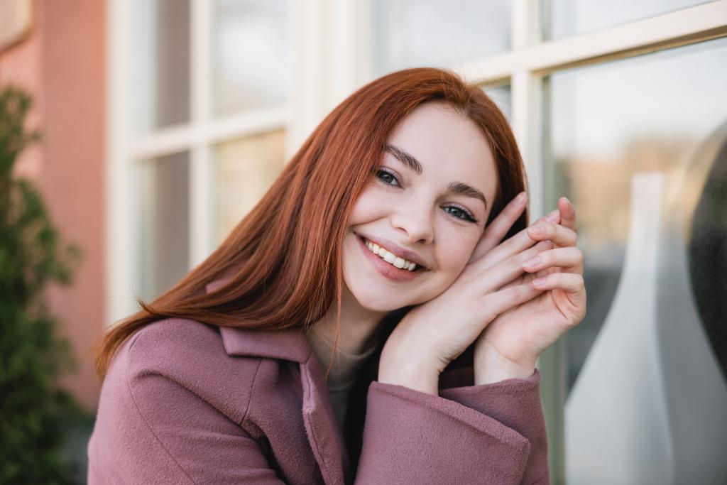 portrait of young cheerful woman in coat looking at camera outside - Photo, image