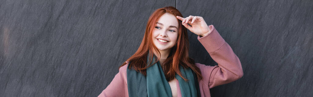 happy redhead woman in scarf smiling near grey marble wall, banner - Foto, imagen
