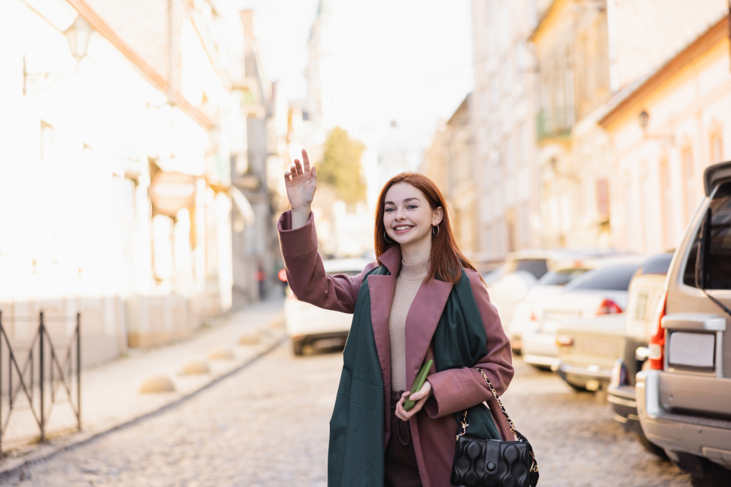 wesoła ruda kobieta w płaszczu wzywa taksówkę na ulicy europejskiej  - Zdjęcie, obraz