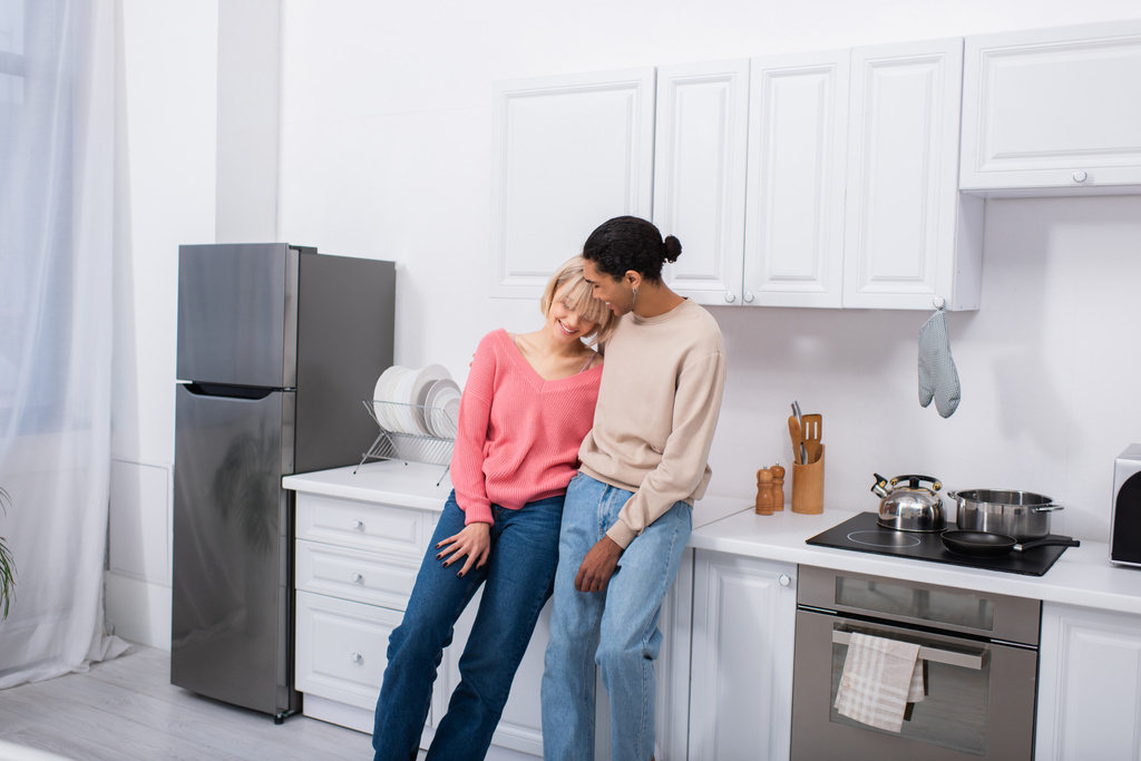 glückliches multiethnisches Paar, das sich in der modernen Küche umarmt  - Foto, Bild