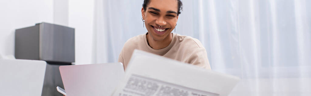 happy young african american man reading newspaper near laptop, banner  - Fotó, kép