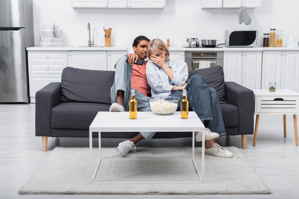 joven interracial pareja viendo miedo película en sala de estar - Foto, Imagen