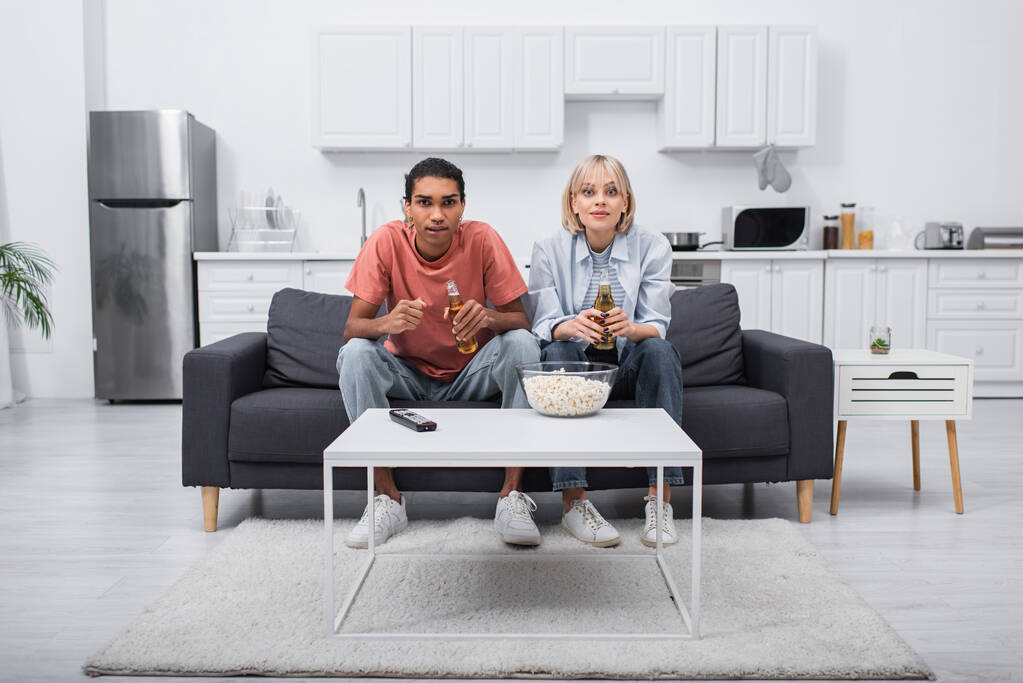 young multiethnic couple cheering while watching sport match in living room  - Foto, imagen
