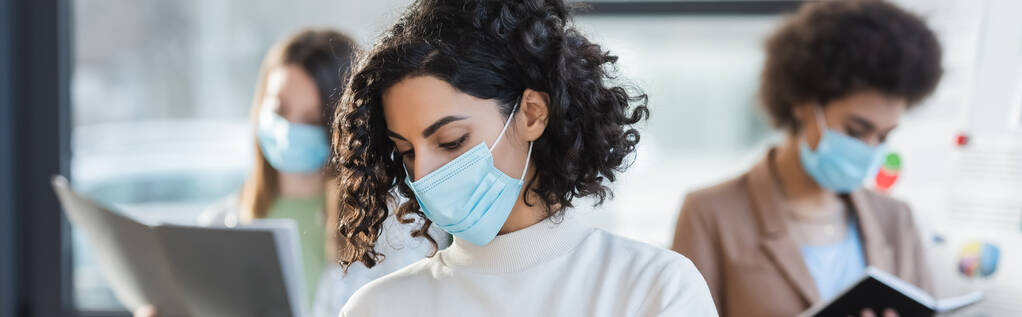Femme d'affaires musulmane en masque médical debout près de collègues flous dans le bureau, bannière  - Photo, image