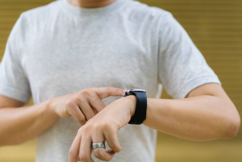 Active Asian young sportsman using a smartwatch or smart fitness band to track his outdoor workout and activities, man reviewing an exercise and health information after finished outdoor workout. - Photo, Image
