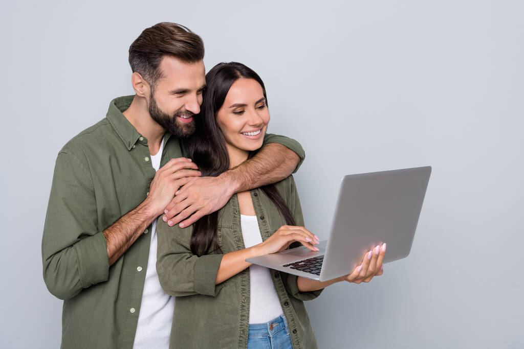 Retrato de pareja alegre tierna atractiva usando el ordenador portátil viendo vídeo aislado sobre fondo de color pastel gris - Foto, Imagen