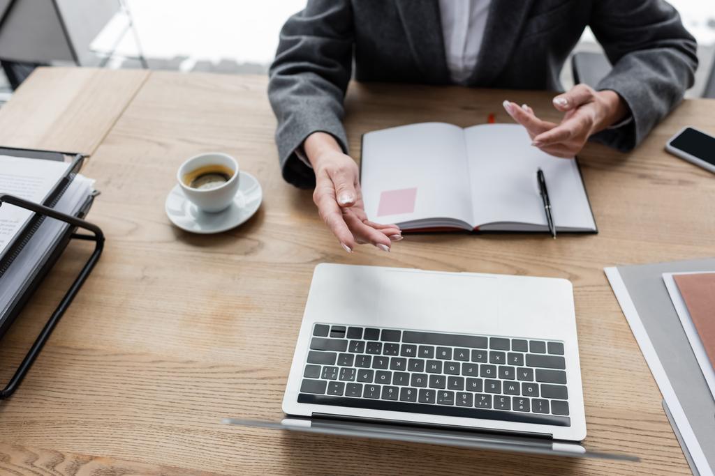 Teilbild eines Bankers, der während einer Videokonferenz auf Laptop neben leerem Notizbuch und Kaffeetasse gestikuliert - Foto, Bild