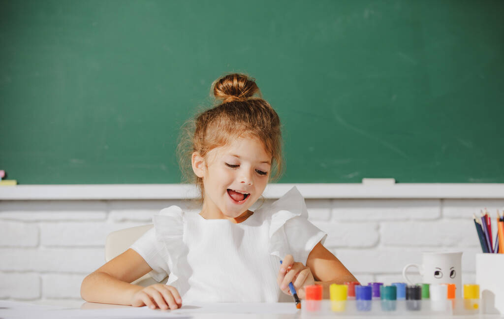 Aranyos kis óvodás lány rajzol az iskolában. Gyerekfestés az általános iskolában. Aranyos iskolás lány rajz az iskolában. - Fotó, kép