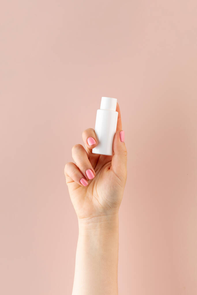 Eine Frauenhand hält einen weißen Schlauch mit einem Kosmetikprodukt auf rosa Hintergrund. Beauty Produktkonzept. Stichprobe. - Foto, Bild