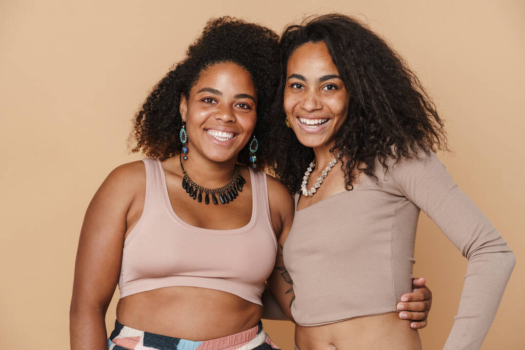 Joven negro dos mujeres abrazando y sonriendo a la cámara aislada sobre fondo beige - Foto, imagen