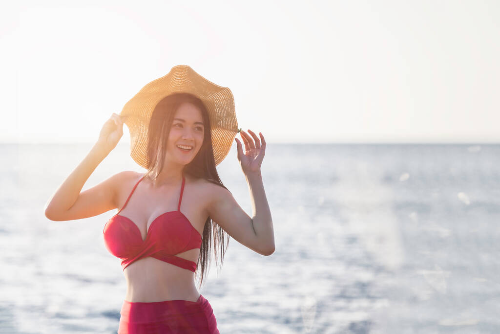 Молода вродлива жінка в одязі з щасливою подорожньою посмішкою йде береговим морем біля блакитної хвилі води під час відпустки. Дівчинка з темної шкіри влітку, щаслива в червоному бікіні, посміхається на заході сонця в koh chang, Таїланд. - Фото, зображення