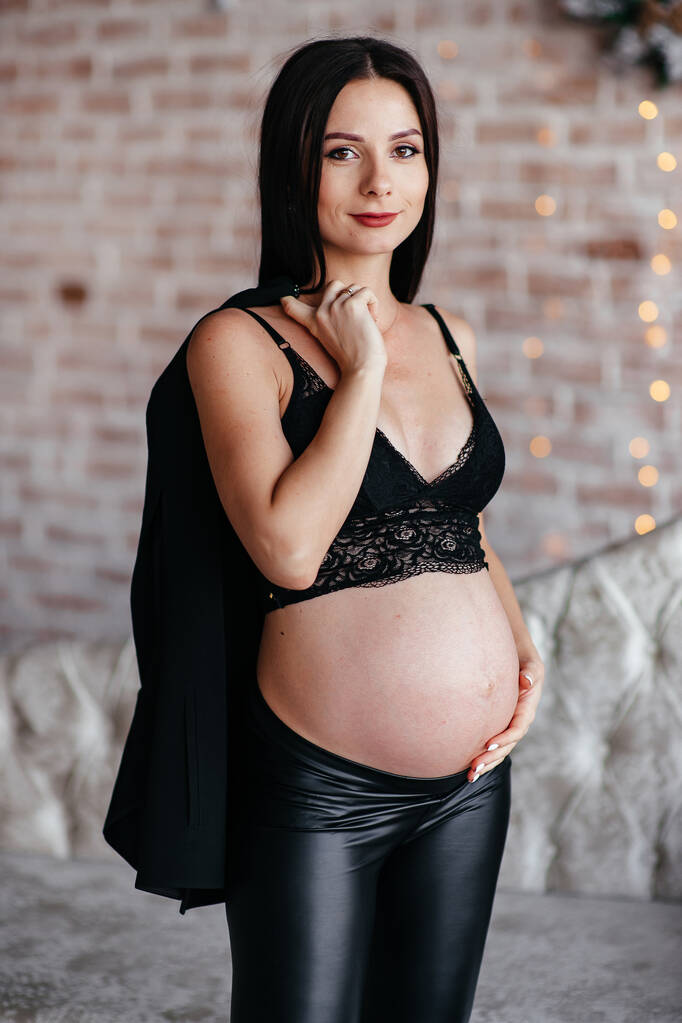 Mujeres embarazadas jóvenes, pelo largo, vestido negro y sombrero posando en studio.Grey fondo. - Foto, imagen